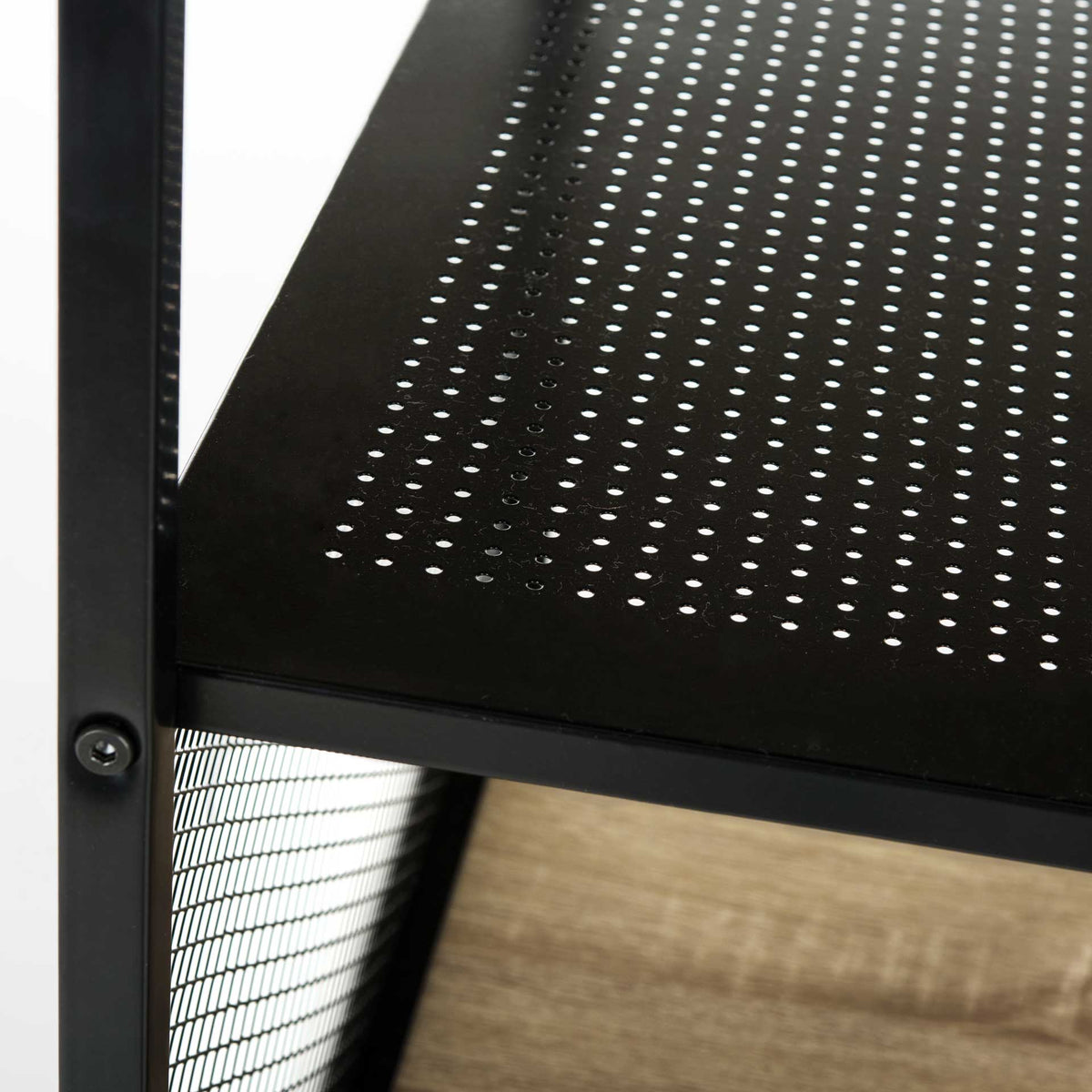 A perforated black metal shelf provides airy storage above the light wood-look desktop