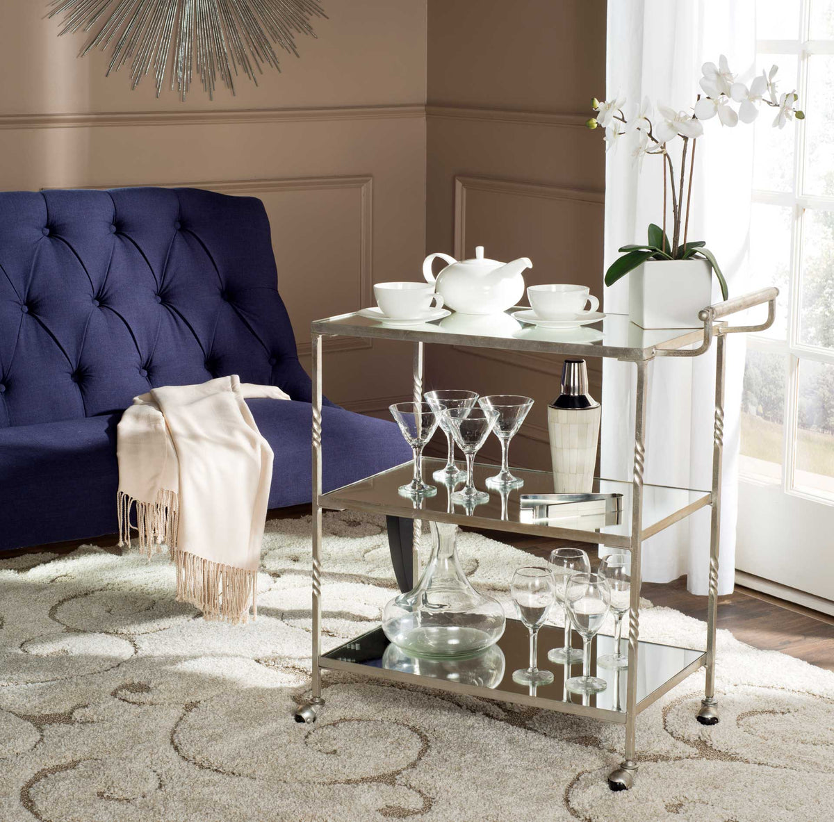 Silver bar cart keeps drinks and glassware close at hand on gleaming mirrored tiers.
