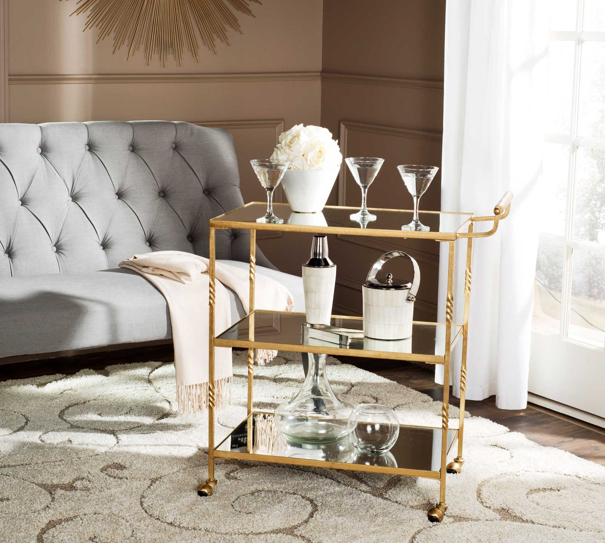 Gold bar cart holds cocktails and serving pieces on three gleaming mirrored surfaces.