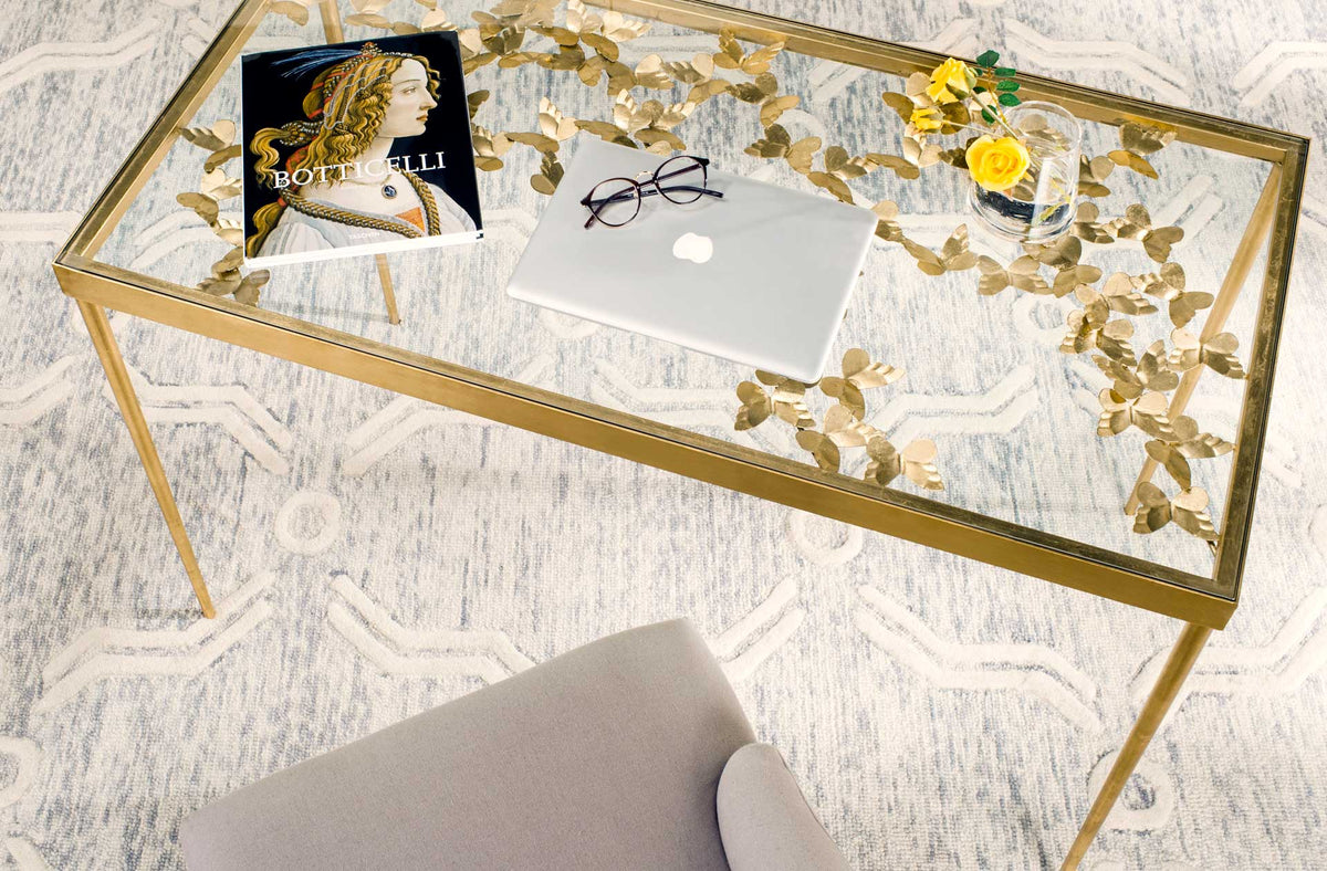 The clear glass desk offers room for a laptop while displaying gold butterflies beneath its surface.