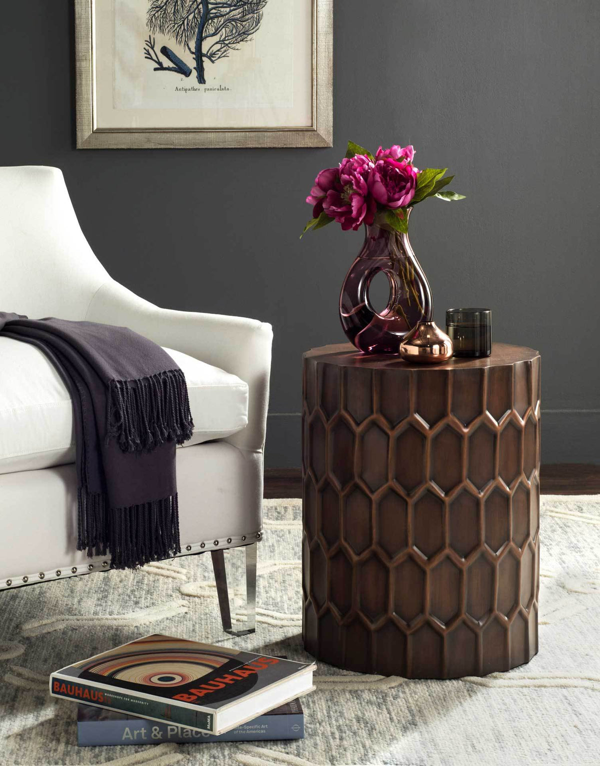Honeycomb-patterned drum table adds antique copper warmth beside a cream upholstered chair