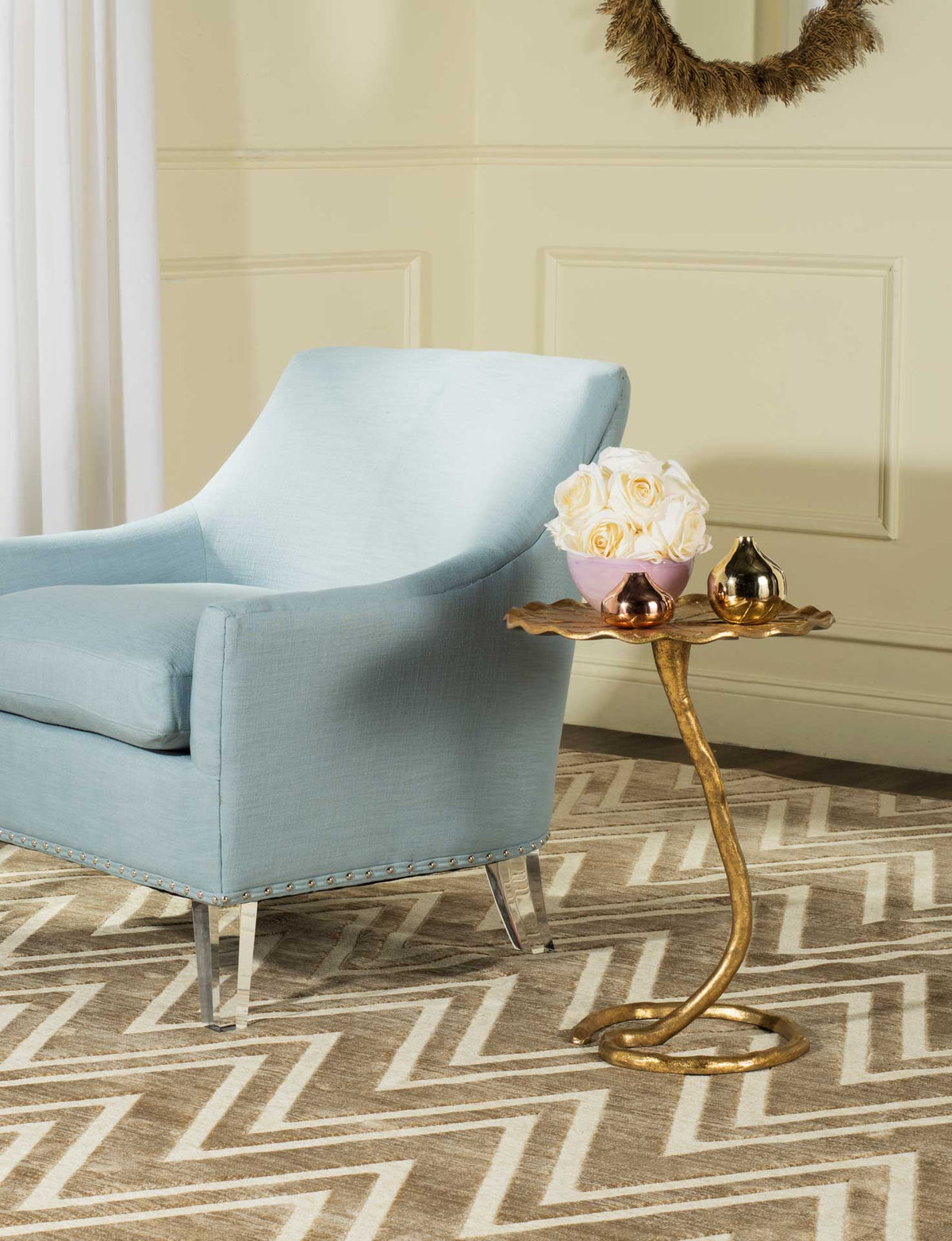 A gold side table with a leaf-shaped top adds sculptural shine beside a pale blue chair