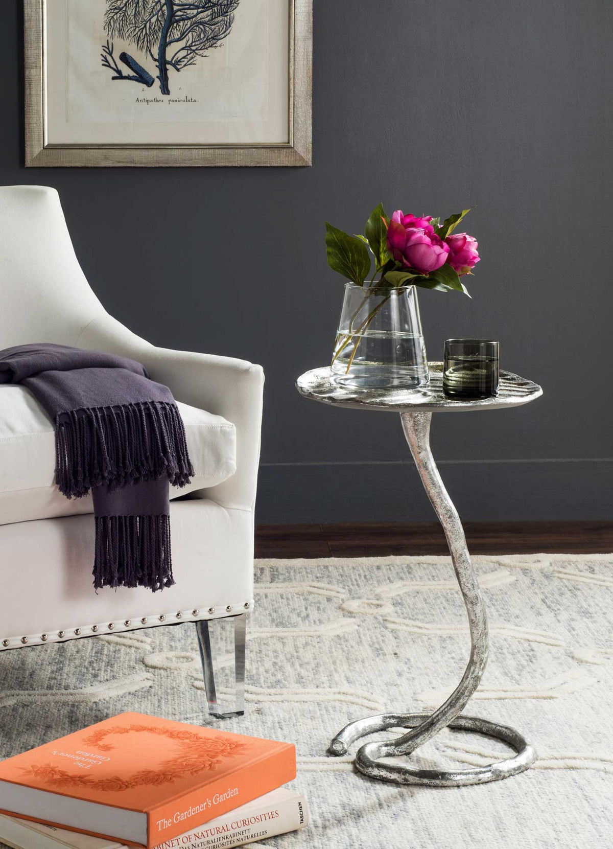 A silver leaf side table adds sculptural flair beside a sofa while holding flowers and a drink.