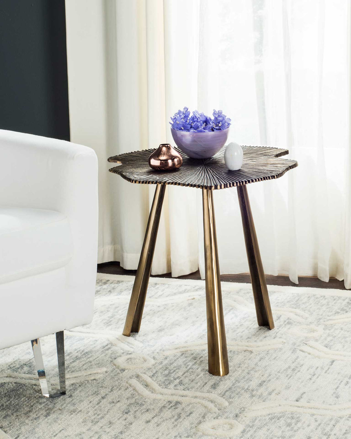 A sculpted leaf side table brings warm metallic texture beside a white chair