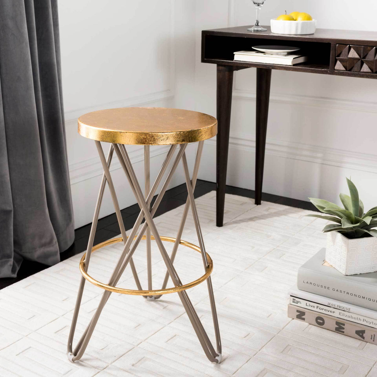 A gold-leaf counter stool with beige crossed legs and a circular footrest adds a warm metallic accent.