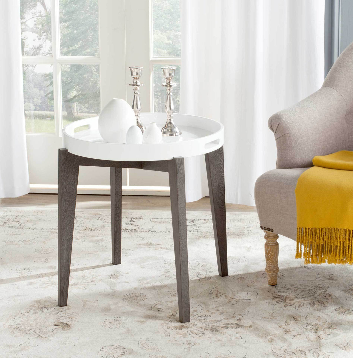 A round white tray top displays decor on a dark brown accent table beside a chair