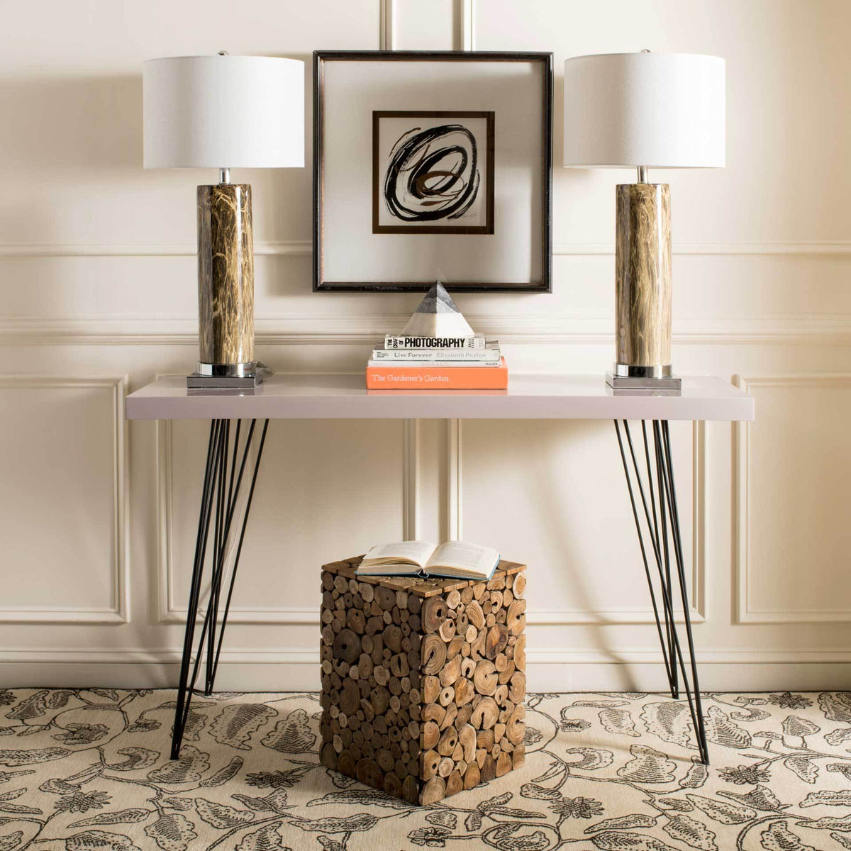 Taupe console table supports twin lamps and books on a sleek top with slim black iron legs.