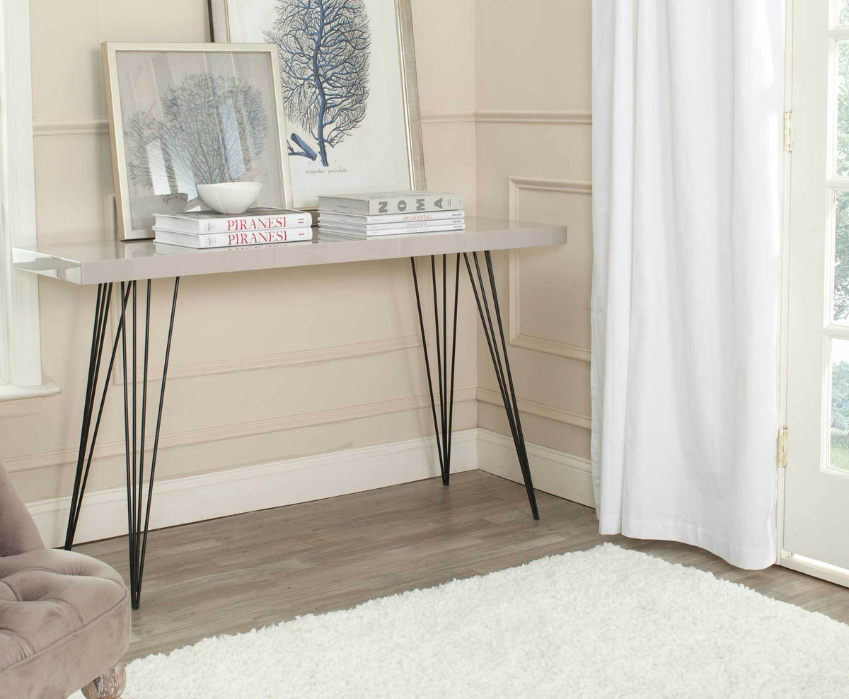 Taupe console table holds stacked books and framed artwork above an open black iron base.