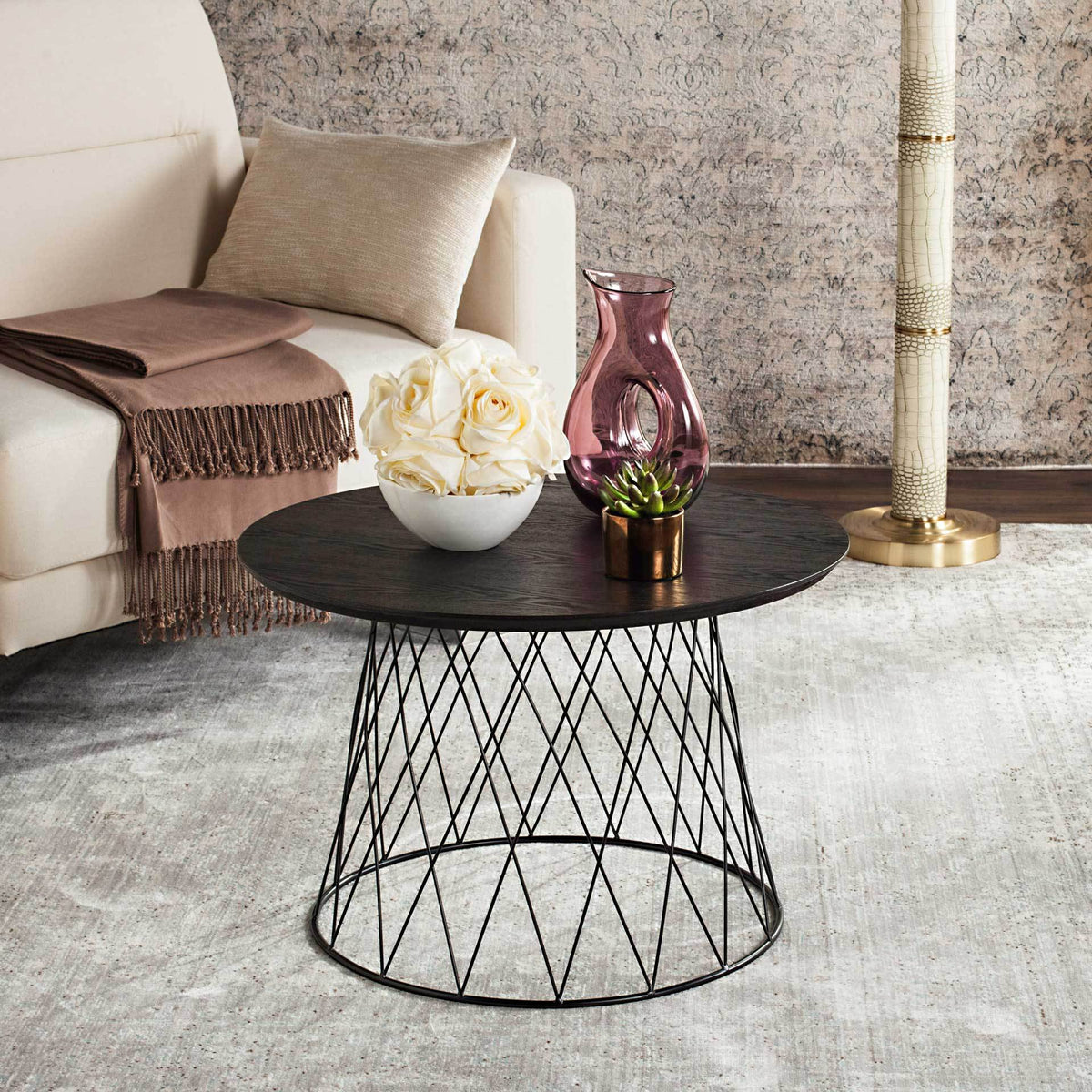 A deep black tabletop and delicate geometric iron base bring bold contrast beside a sofa.