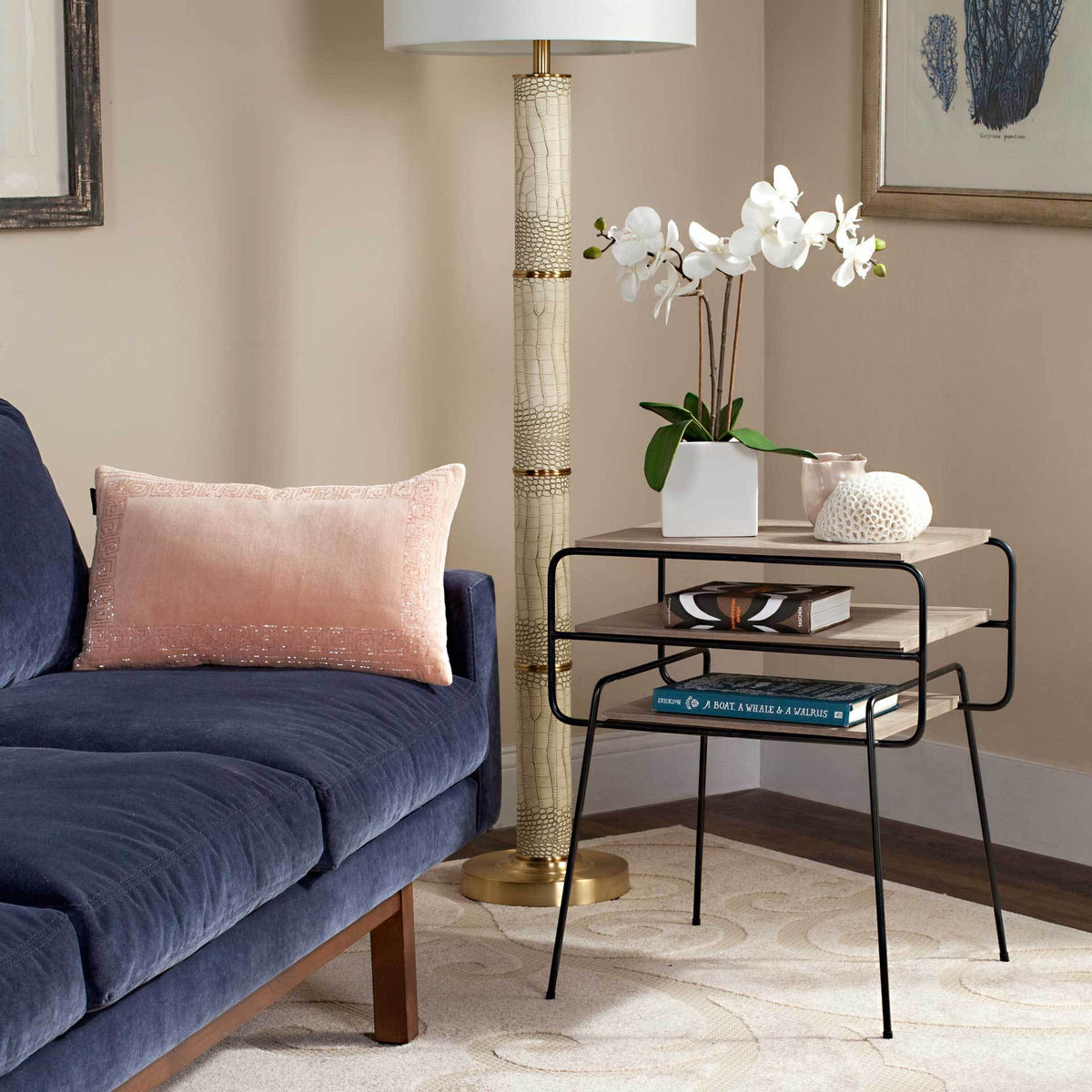 A three-tier end table with light wood-look shelves keeps books and decor close beside a sofa.