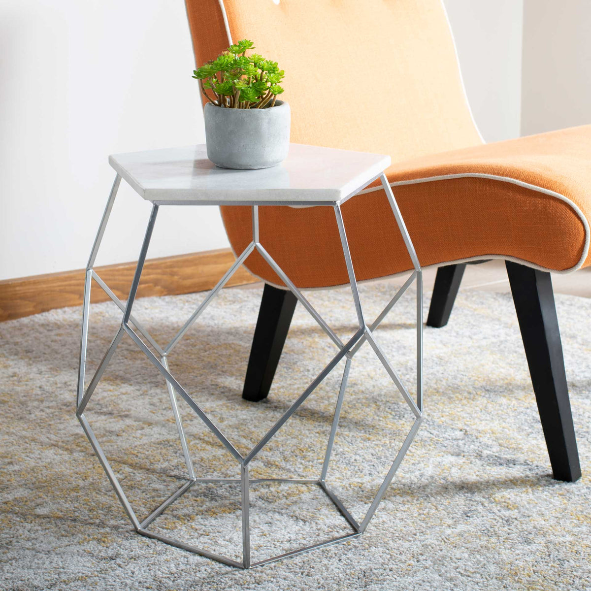A light marble top and silver geometric base add sculptural style beside a lounge chair.
