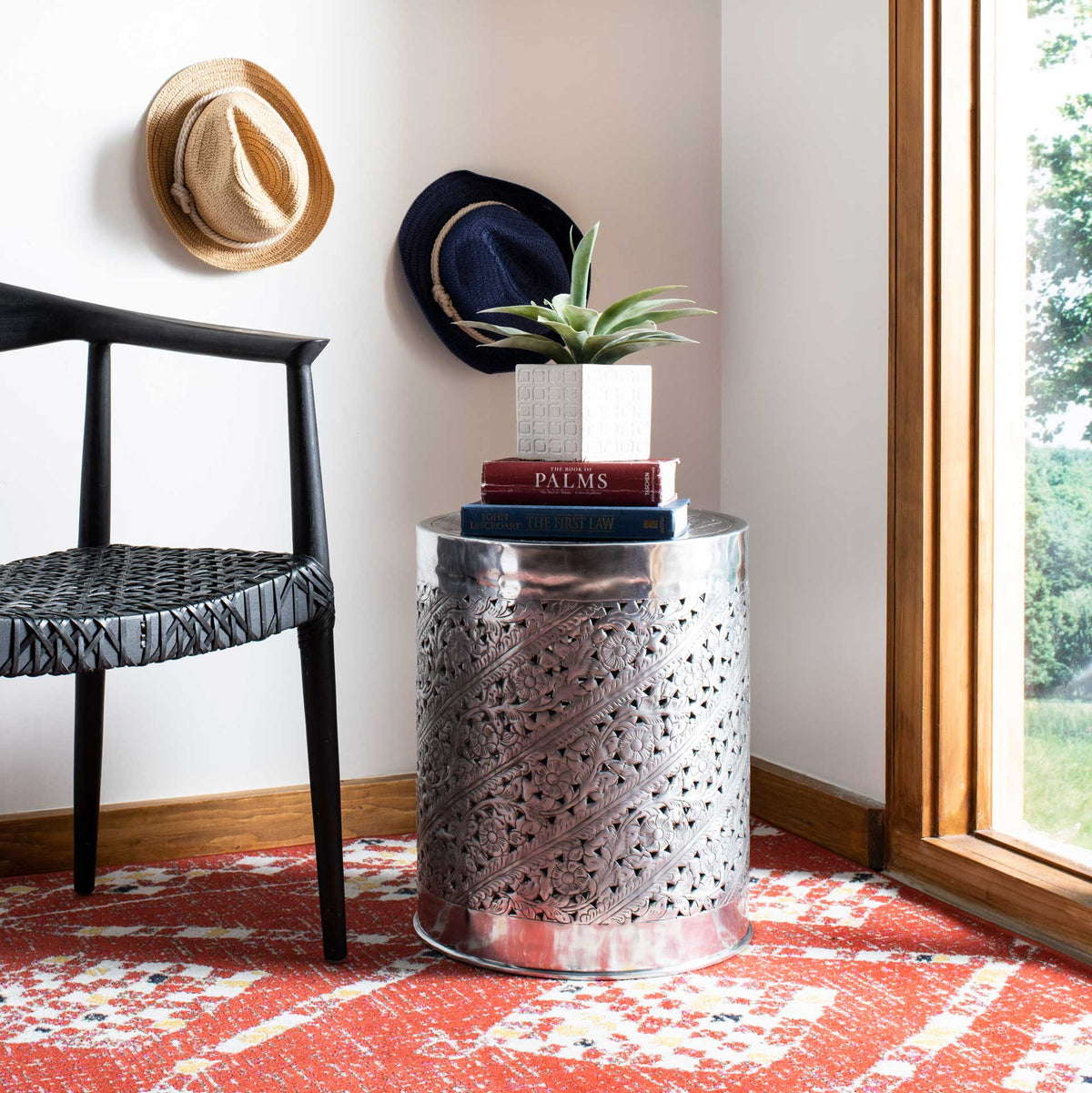 Ornate silver end table holds books and a potted plant beside an accent chair.