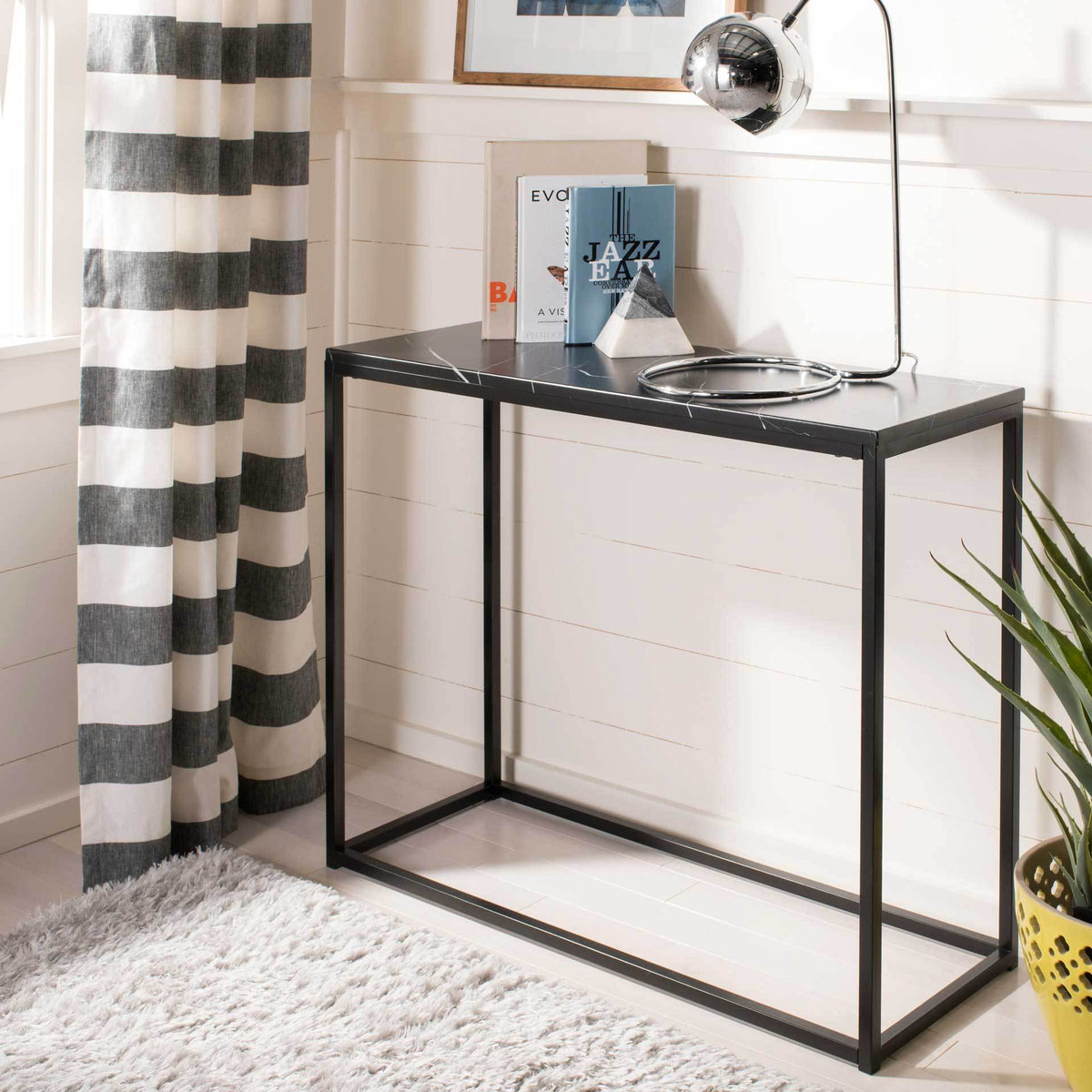 Black console table holds books and a chrome lamp on its white-veined top