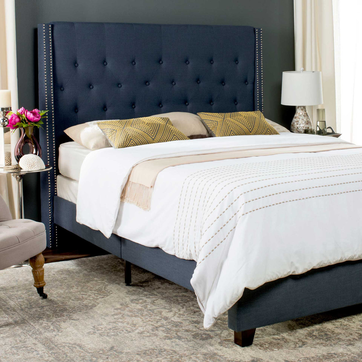 A tall navy headboard pairs plush button tufting with nailhead-lined edges for a tailored look.