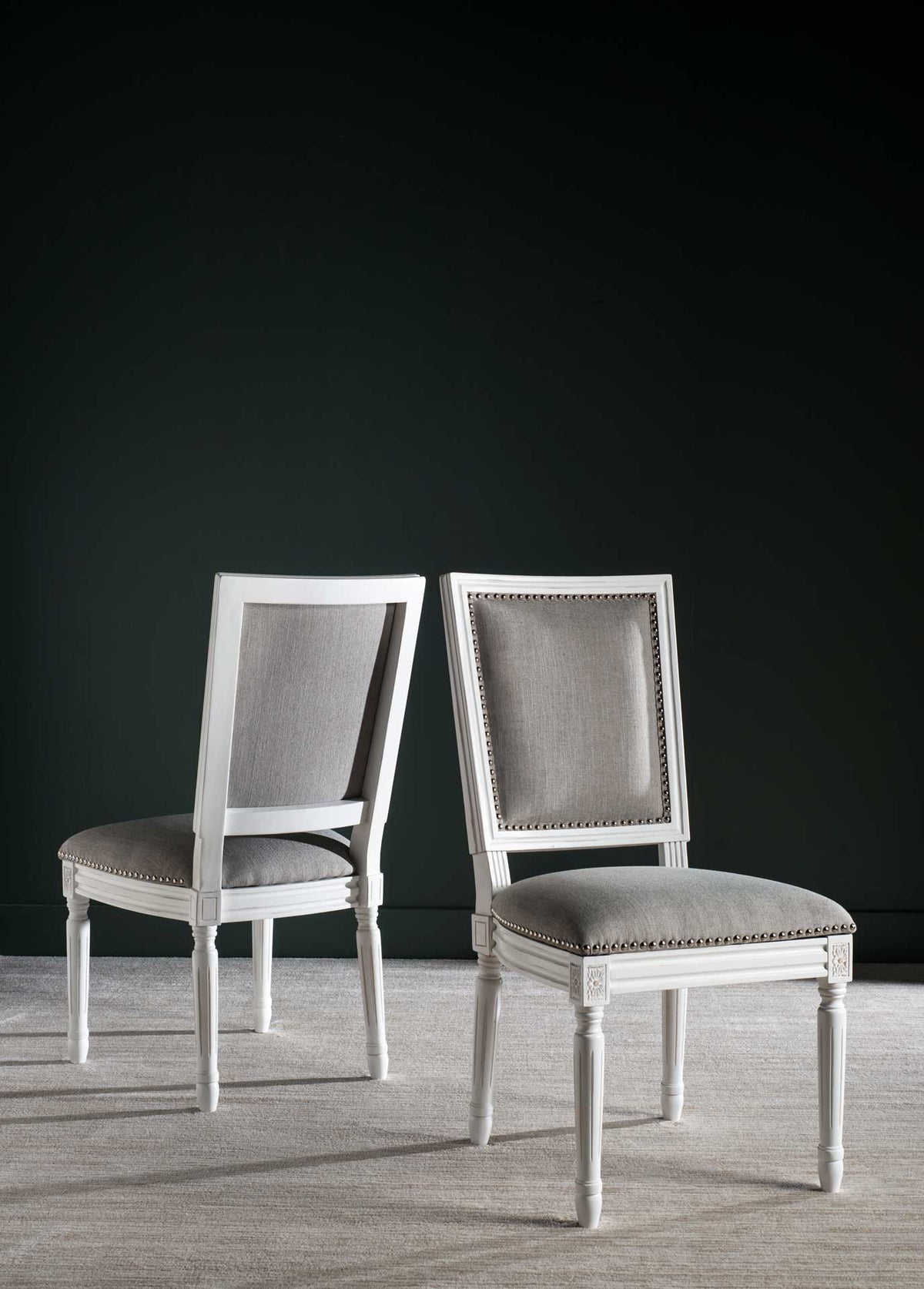 A pair of gray linen dining chairs combines silver nailhead trim with cream wood frames.