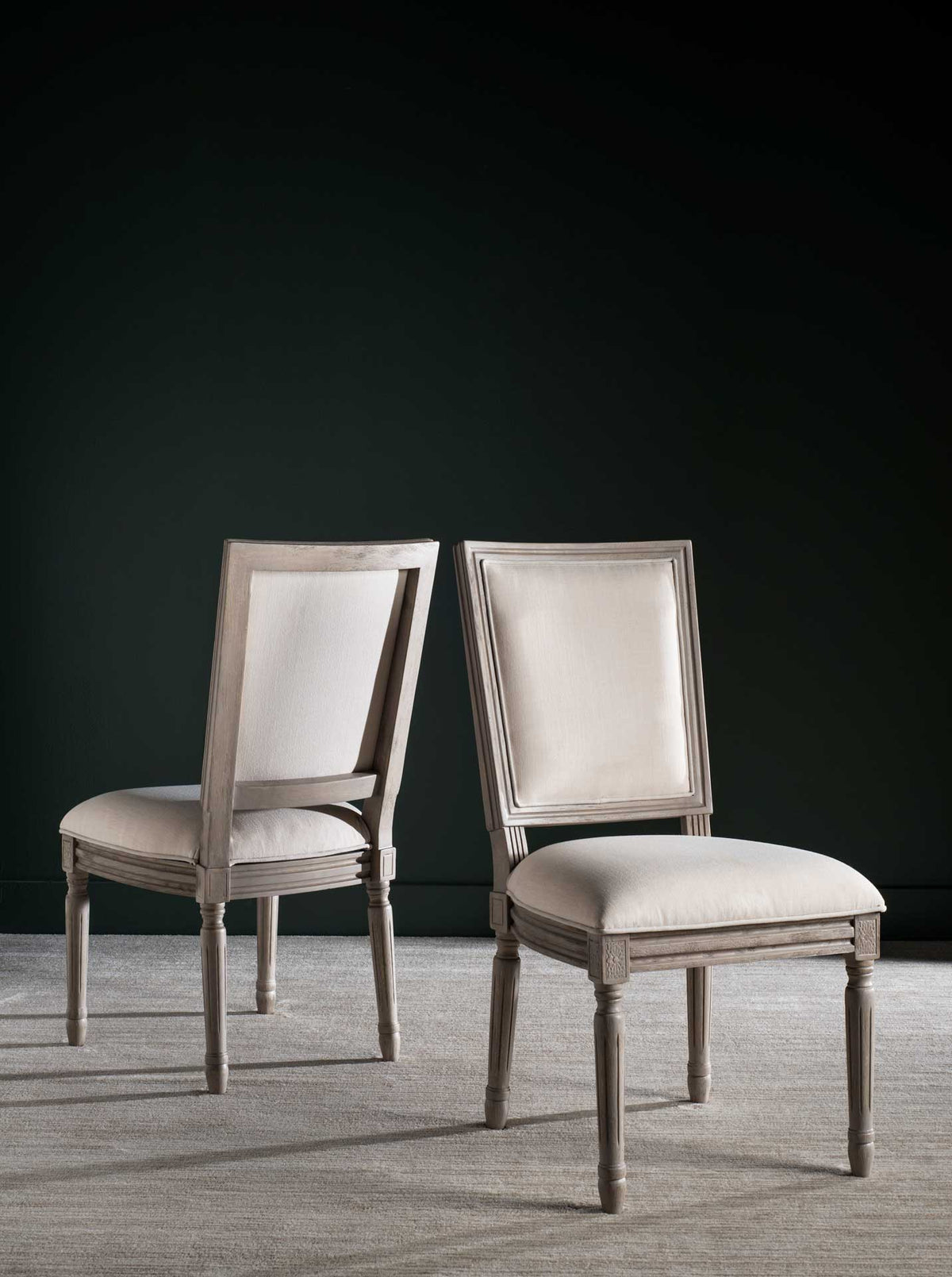 Two linen side chairs pair plush beige seats with gracefully carved gray wood frames.