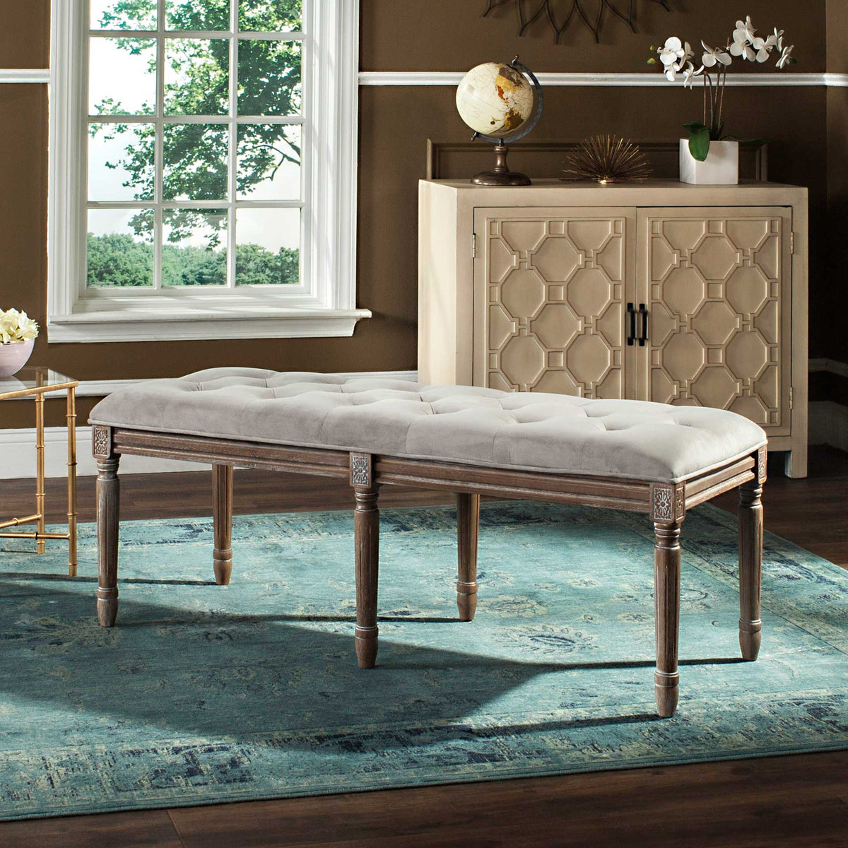 A tufted gray velvet cushion pairs with carved wood details and turned legs for timeless charm