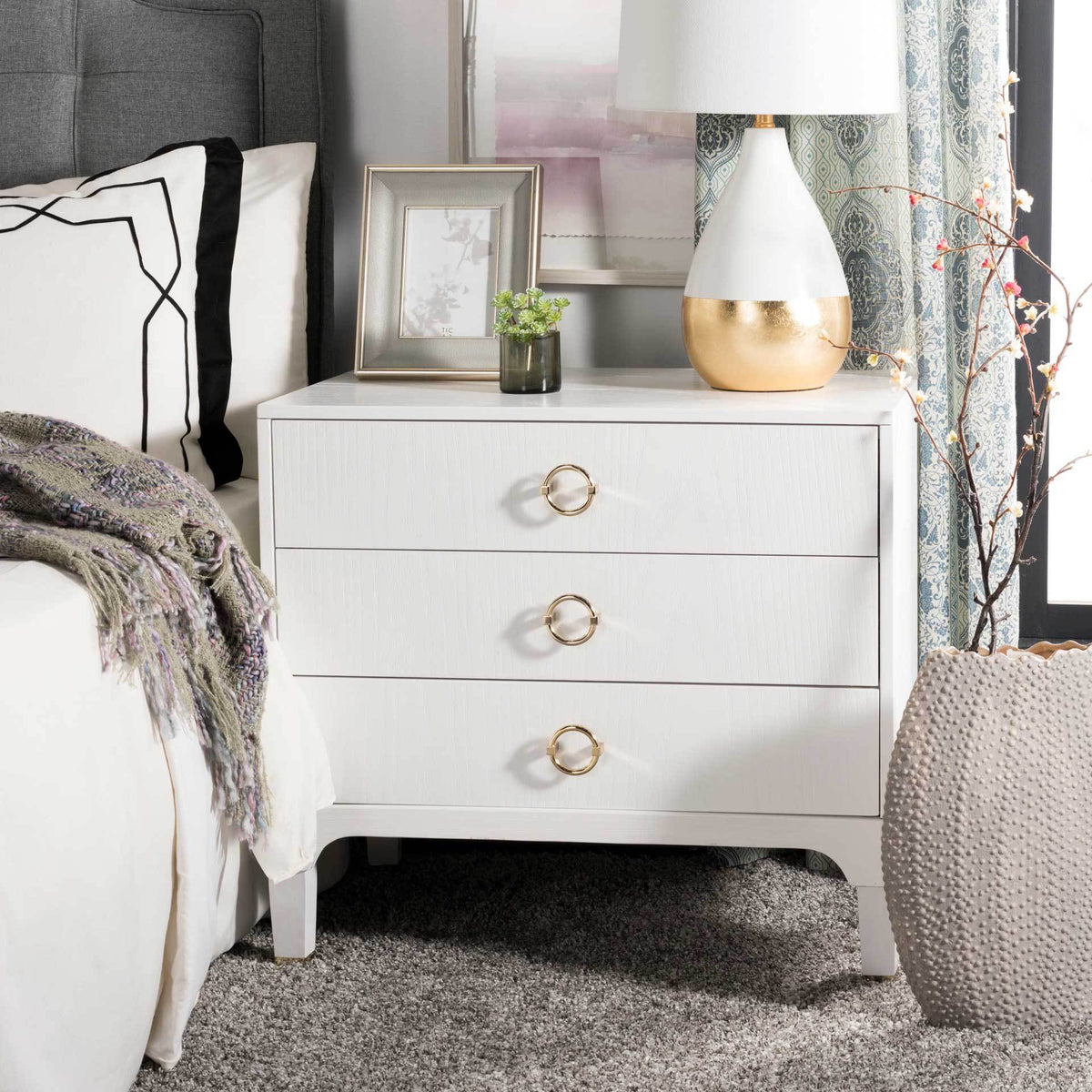 Crisp white nightstand with three drawers and gleaming gold ring pulls brightens the bedside