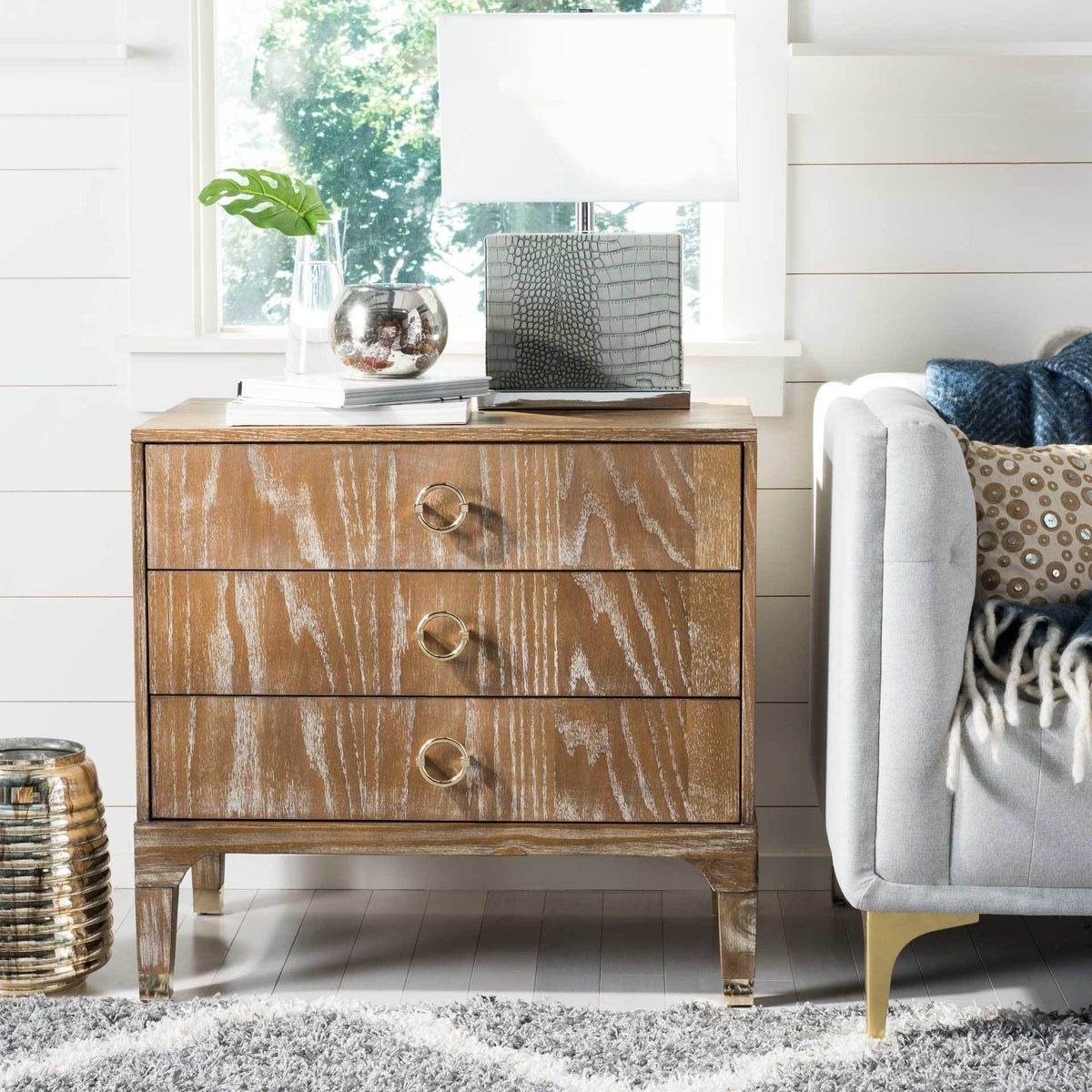 Distressed wood grain and brass ring pulls lend character to this three-drawer nightstand
