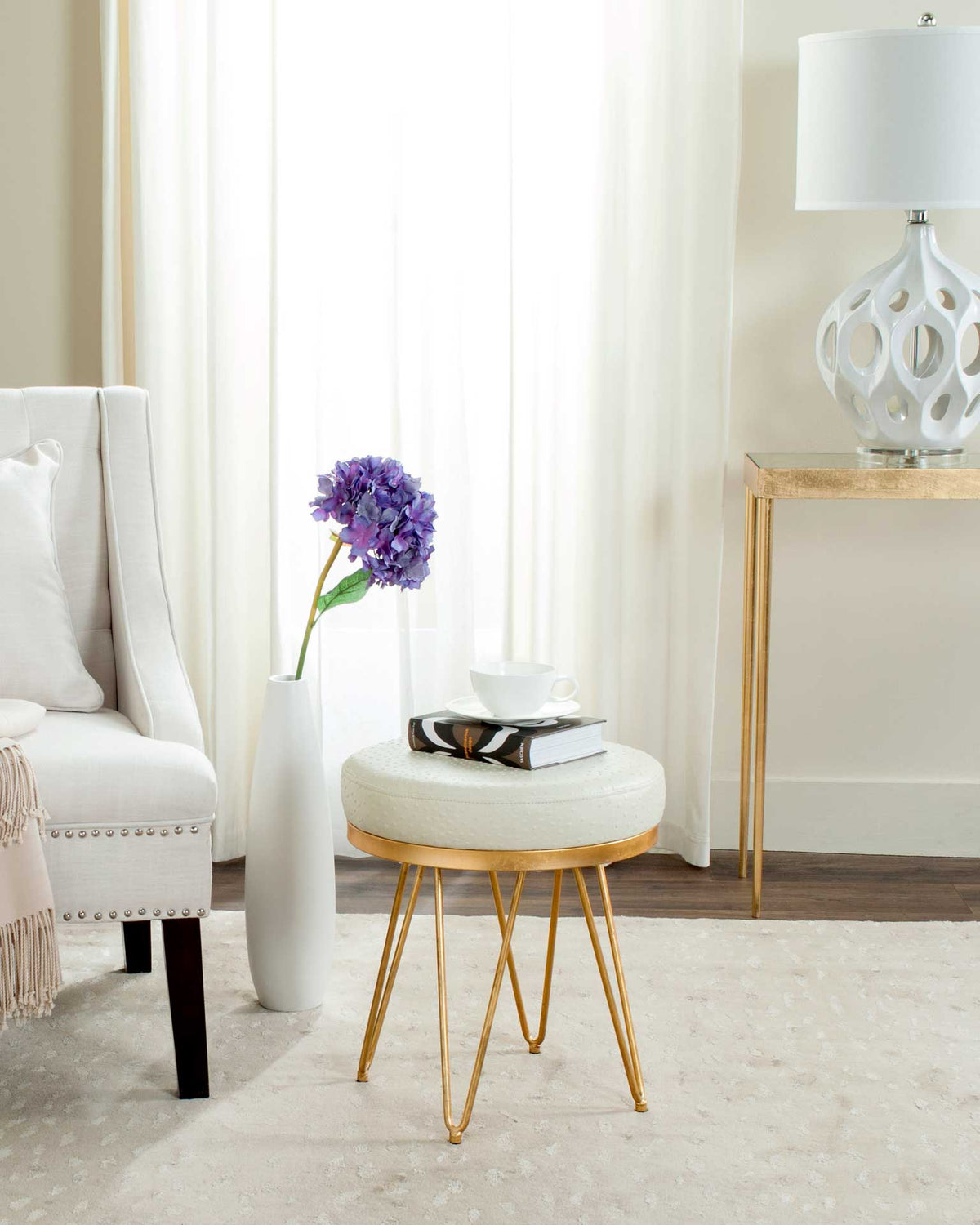 Round cream bench doubles as a stylish perch for books on slender gold-tone legs