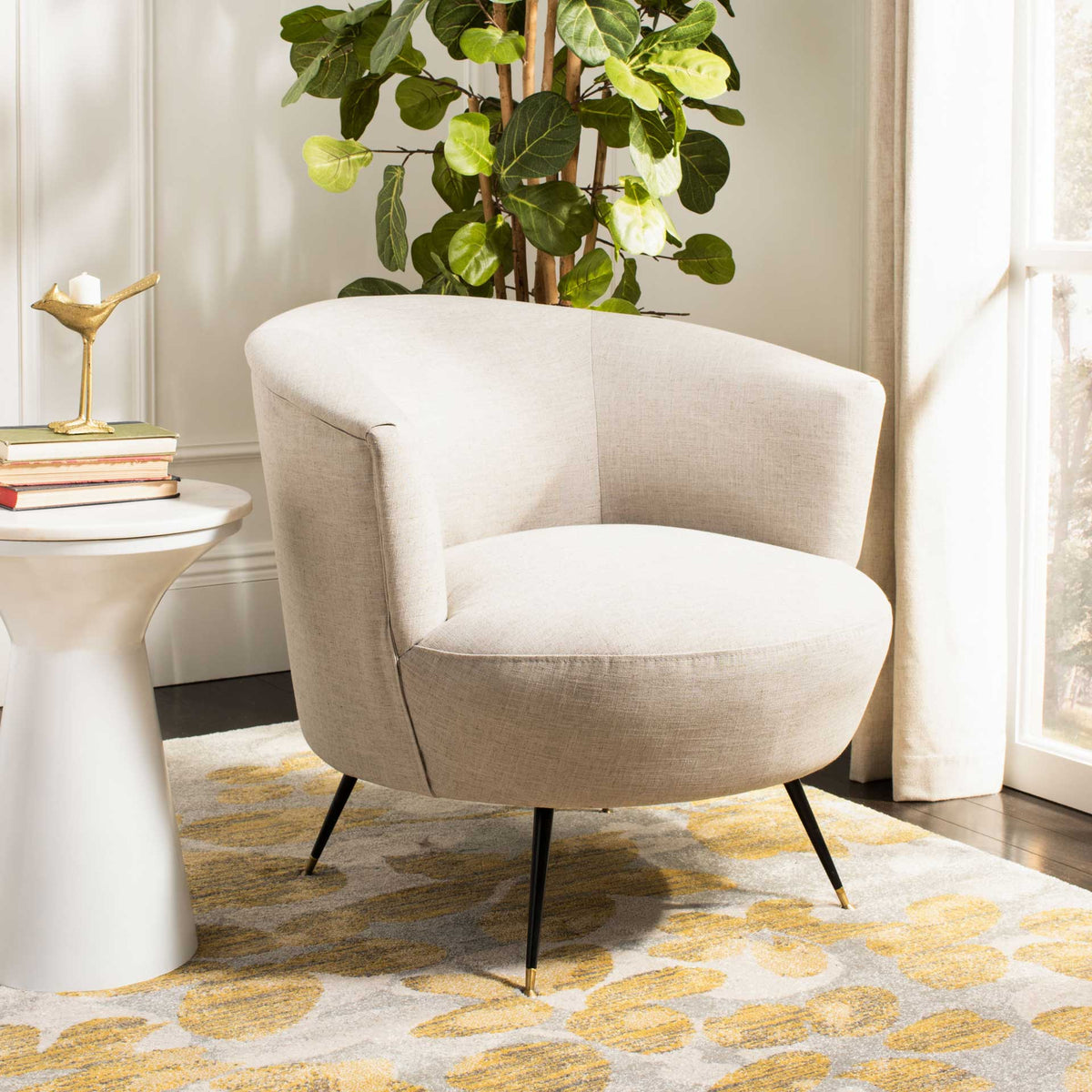 A light gray linen accent chair brings a plush rounded seat, curved arms, and gold-accented legs to the room.