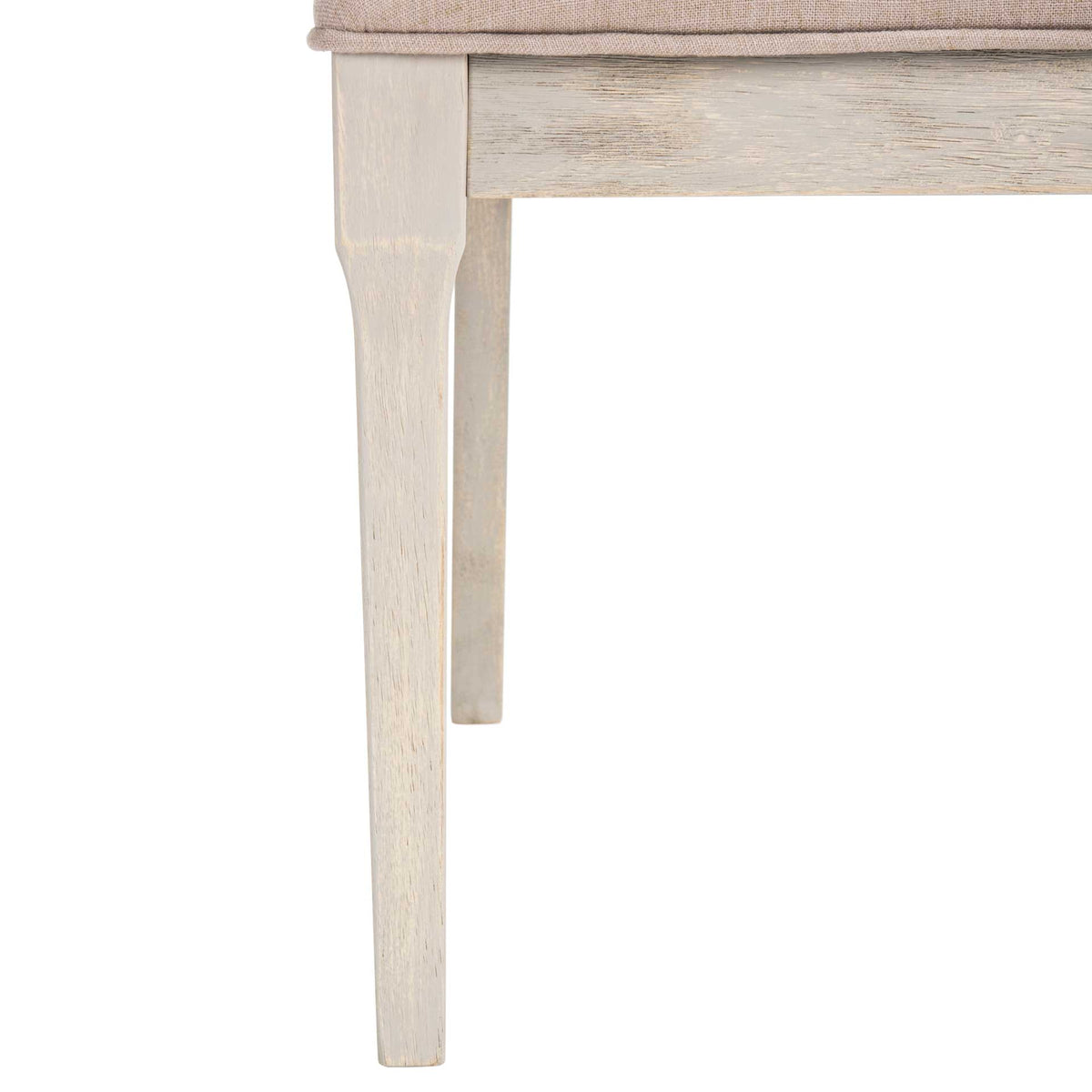 Lightly distressed wood legs taper beneath the soft taupe upholstered seat