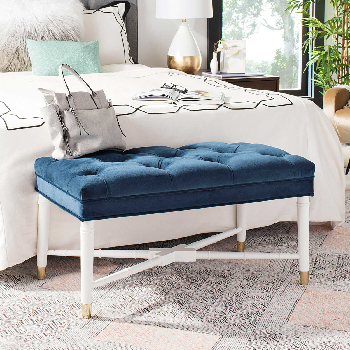 A tufted navy velvet bench adds plush color beside the bed on white brass-capped legs