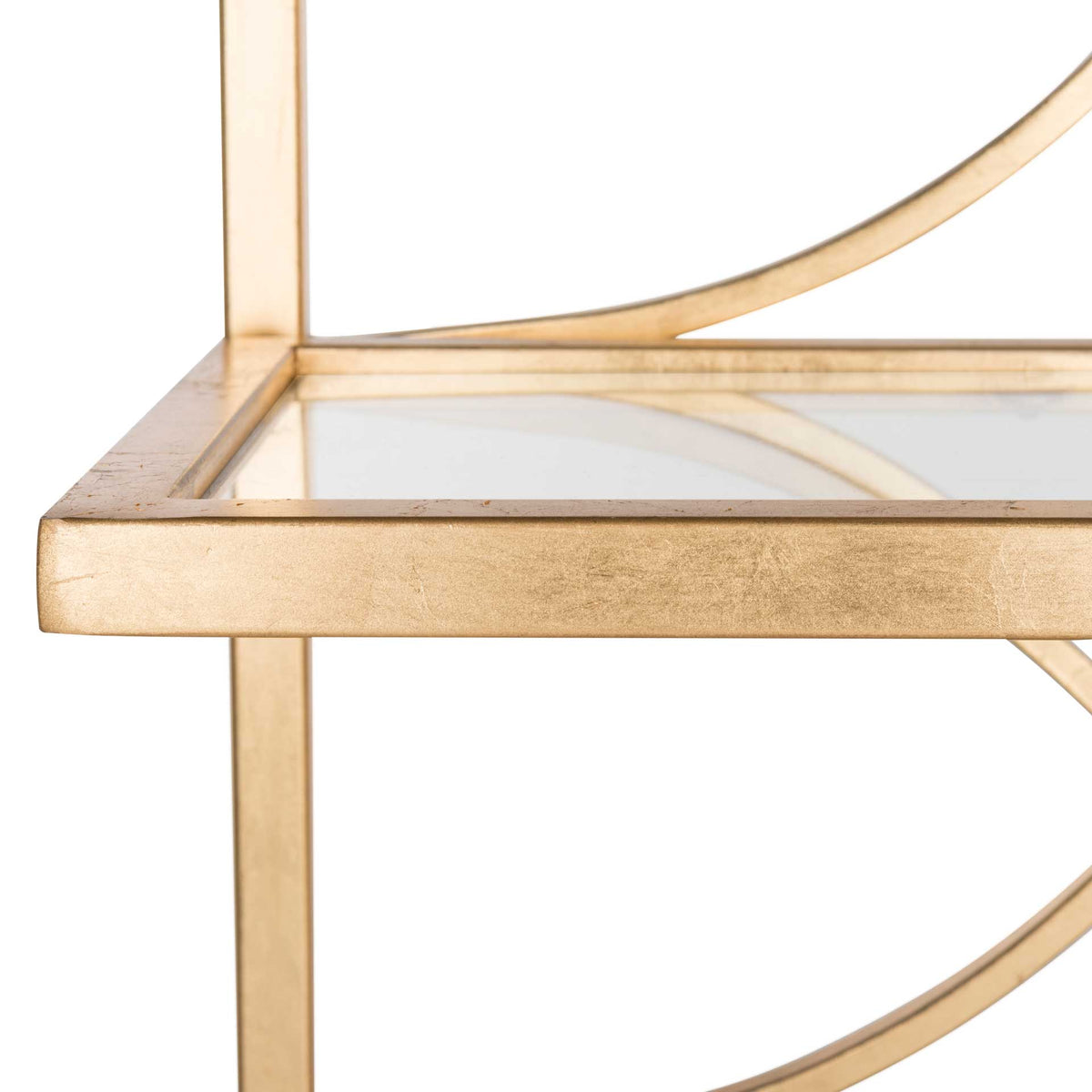Gold-toned edging borders a clear glass shelf beside graceful curved metalwork.