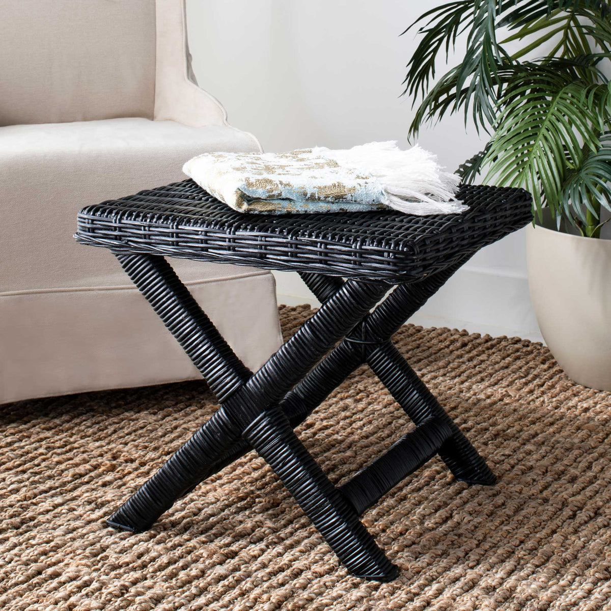 Black woven ottoman adds texture and sculptural X-shaped legs beside a sofa.