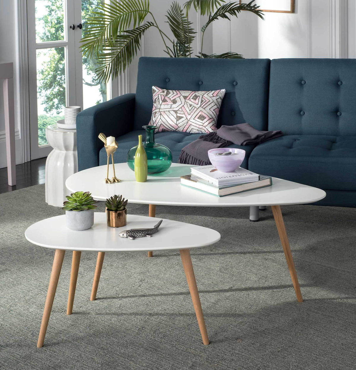 Books and greenery fill the layered white tables, each supported by warm oak legs