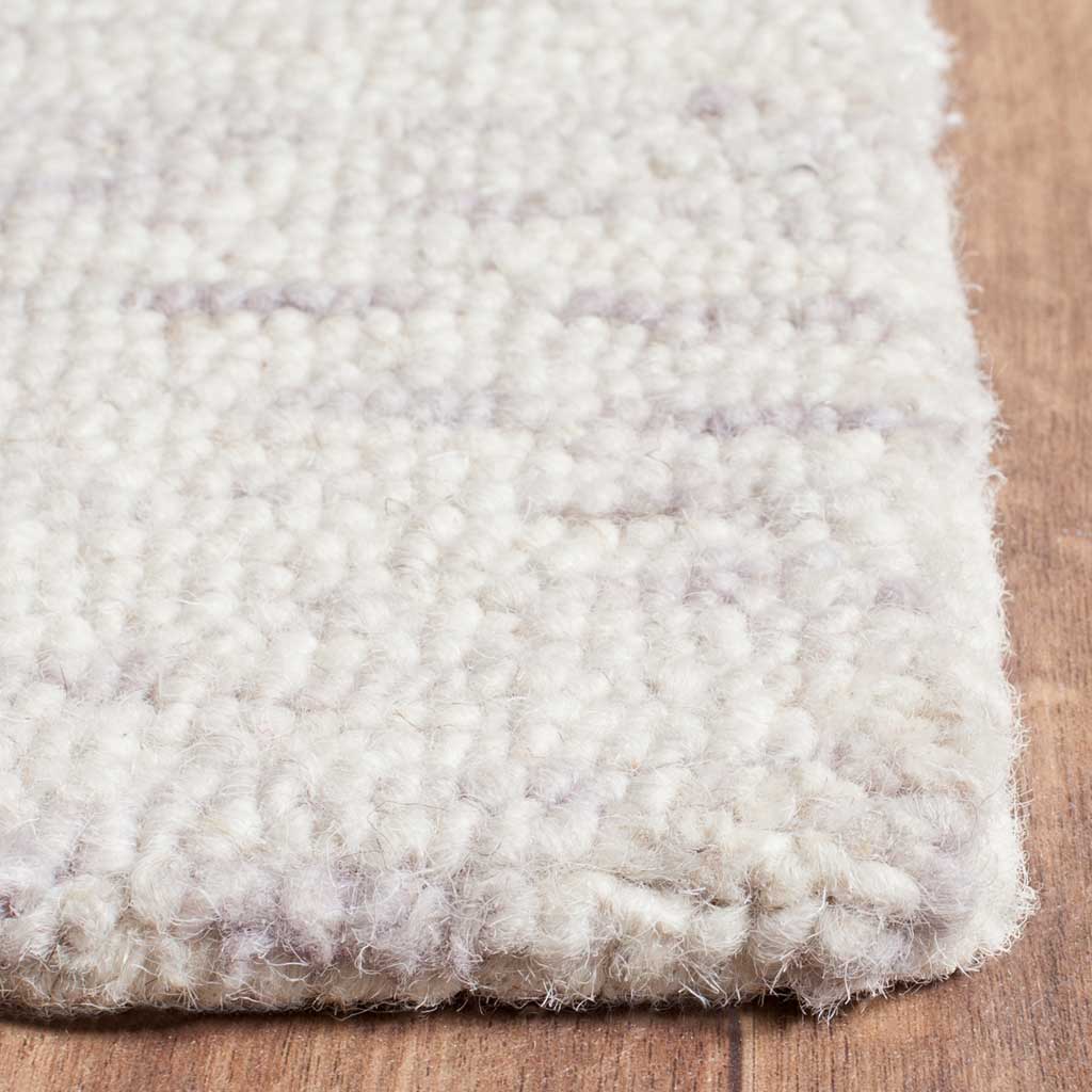Soft ivory wool loops and faint silver flecks define the rug's tidy finished edge