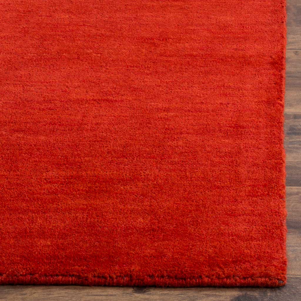 Dense red fibers and a neatly finished edge show the rug's inviting texture