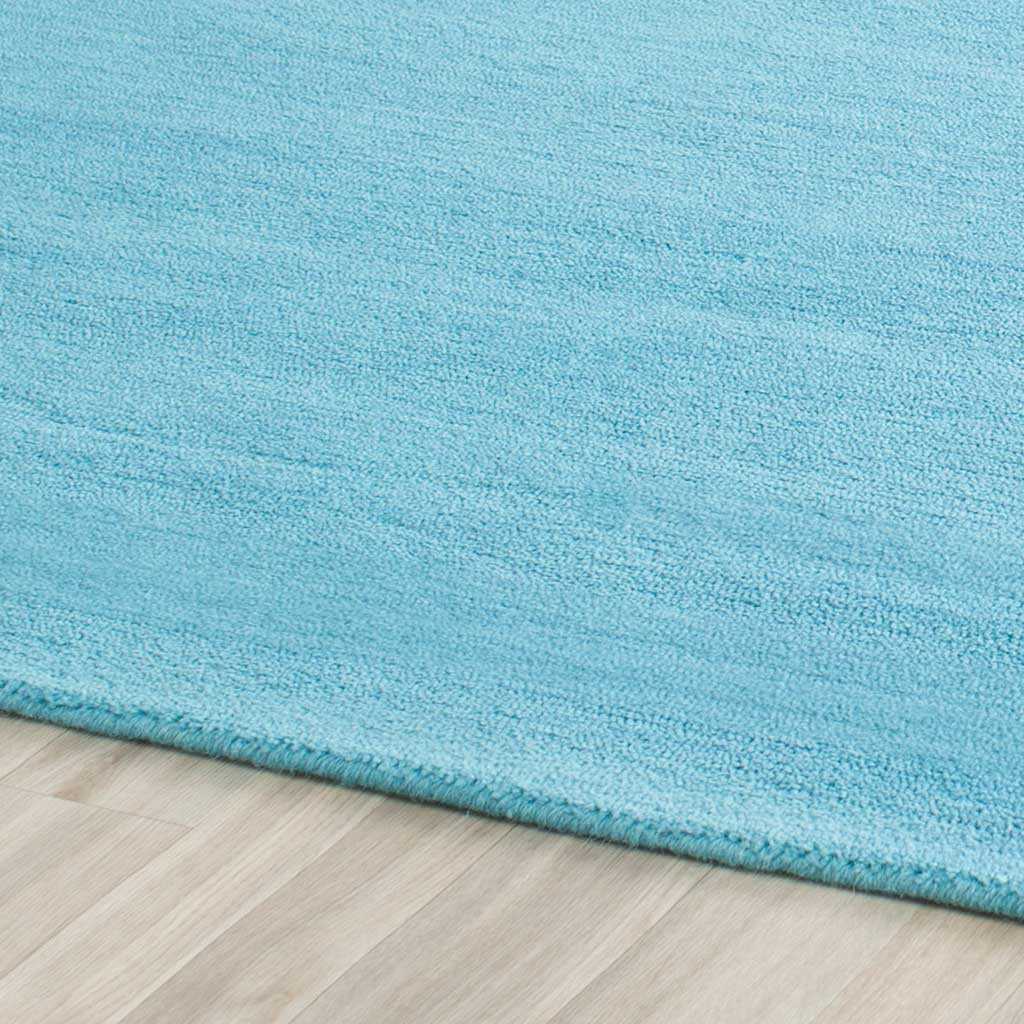 Soft turquoise pile with fine tonal shifts meets a neatly finished rug edge