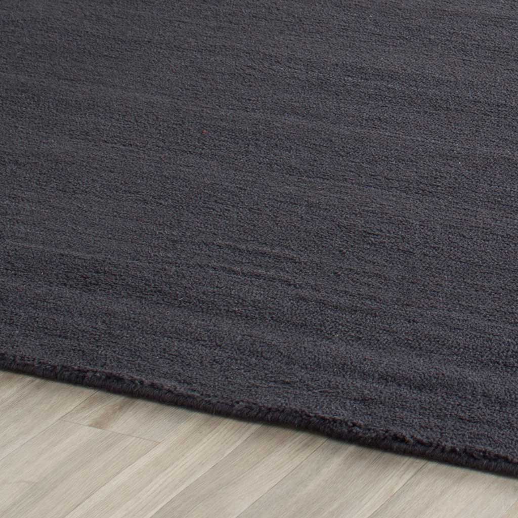 A neat bound edge finishes the charcoal-black rug's dense, softly shaded pile