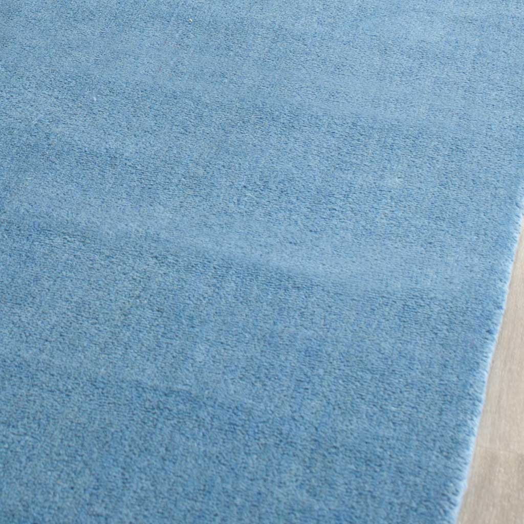 The blue rug's dense pile shows gentle color variation beside its finished edge