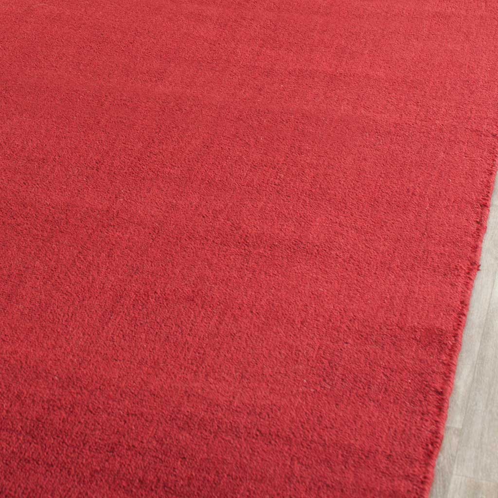 The red rug's smooth pile shows subtle color shifts beside a neatly finished edge