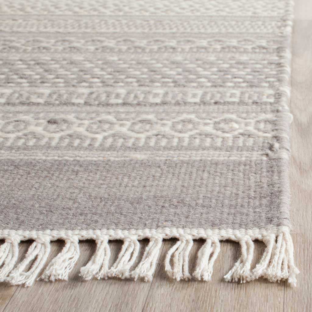 Ivory tassel fringe complements the rug's textured gray weave and intricate motifs.