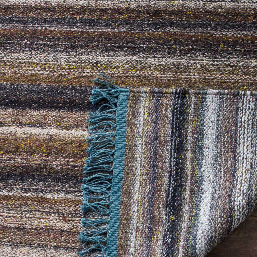 A folded edge displays the rug's woven underside, blue fringe, and richly mottled stripes