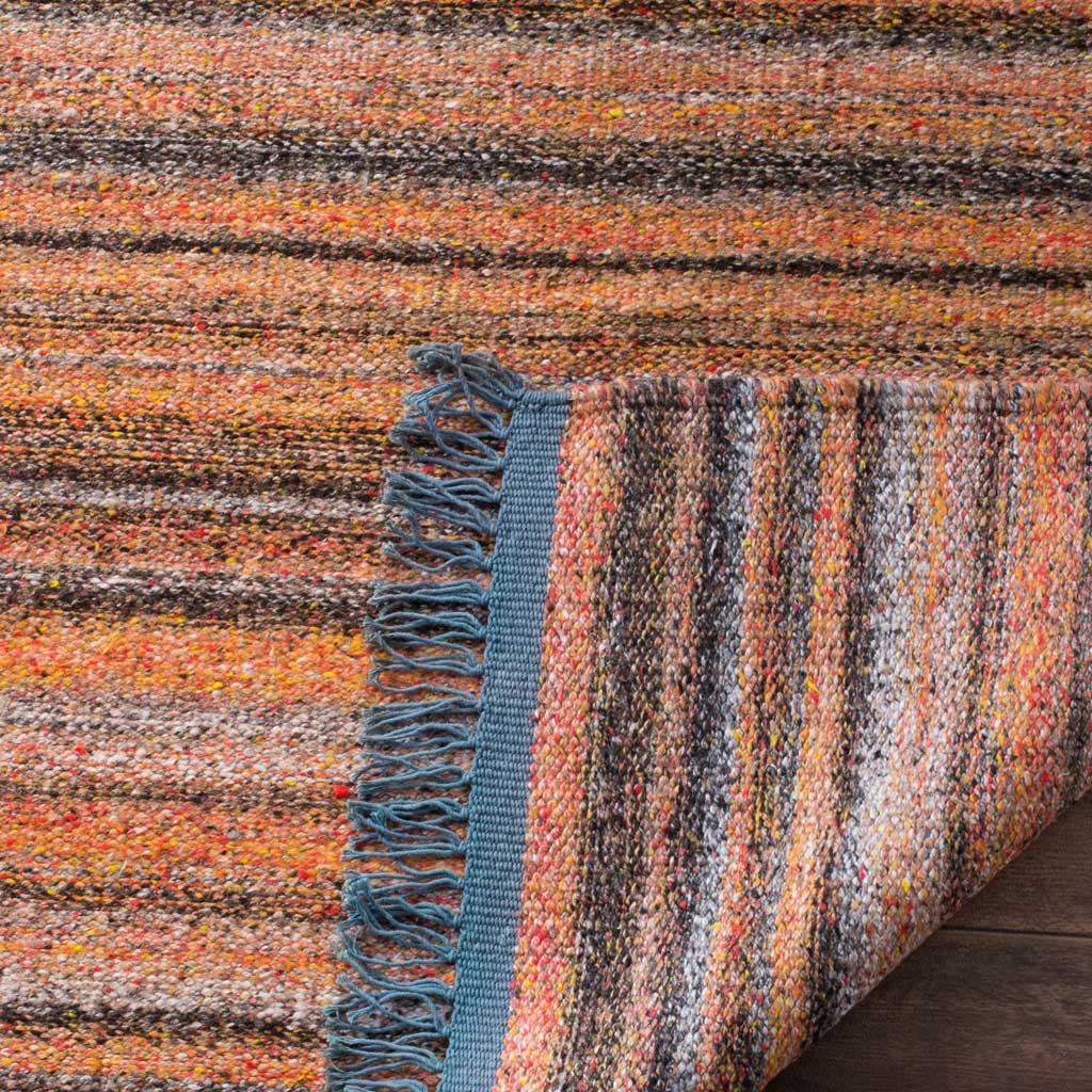 A folded corner exposes the tightly woven underside beside blush stripes and blue fringe
