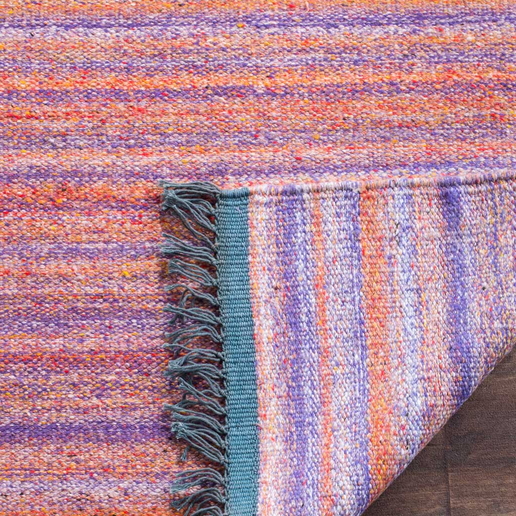 A folded edge reveals the rug's tightly woven underside beside violet stripes and blue fringe