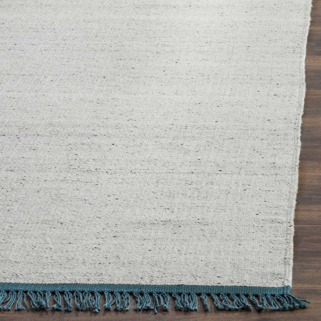 Ivory fibers with tiny gray flecks meet teal fringe along the rug's edge.