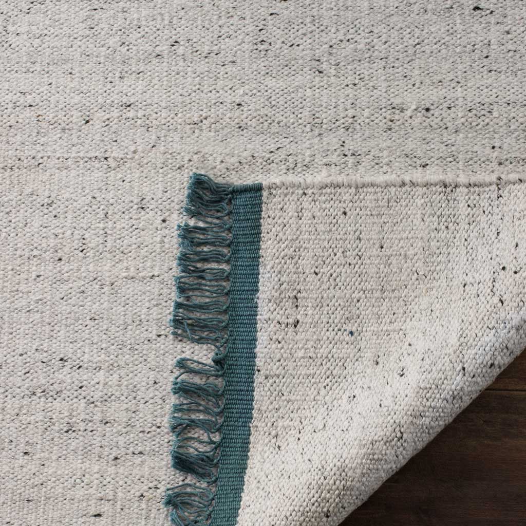 A folded edge reveals the rug's textured woven underside and teal fringe.