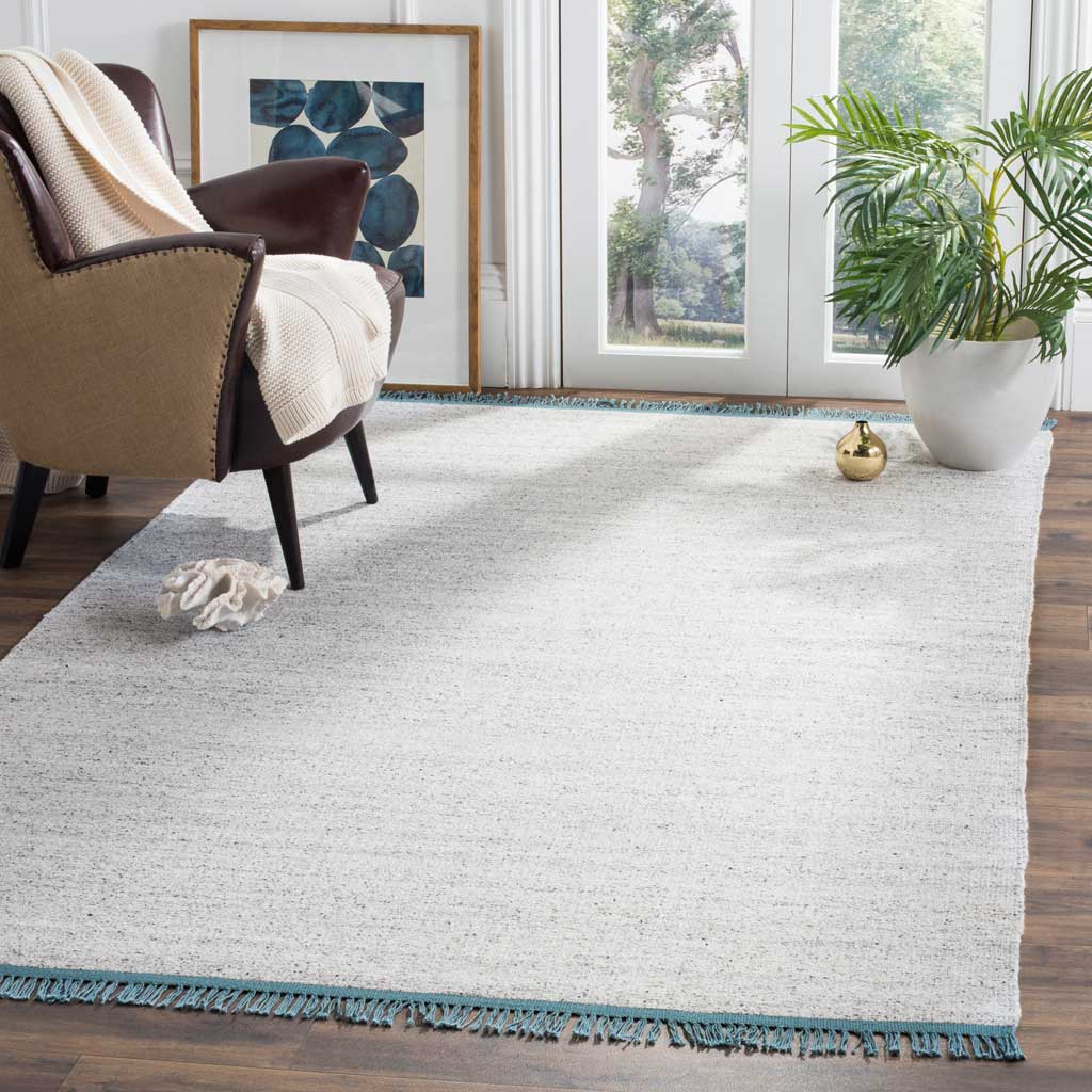 A low-profile gray and ivory rug adds subtle texture and teal-fringed edges to a living space