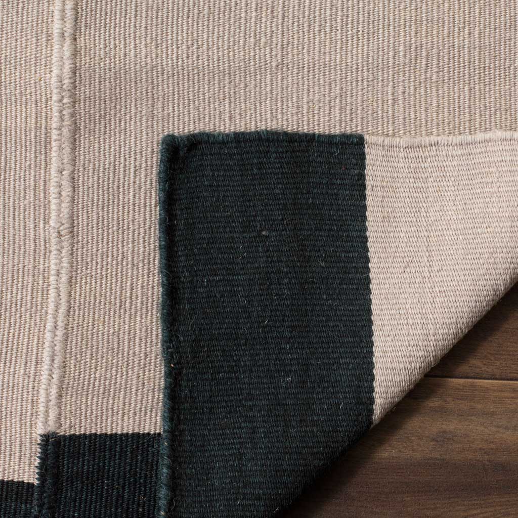The wool rug's woven underside pairs with bold black edging and a neatly finished corner