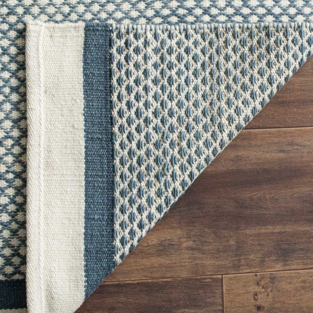 A folded edge reveals the blue and ivory rug's woven backing and contrasting border.