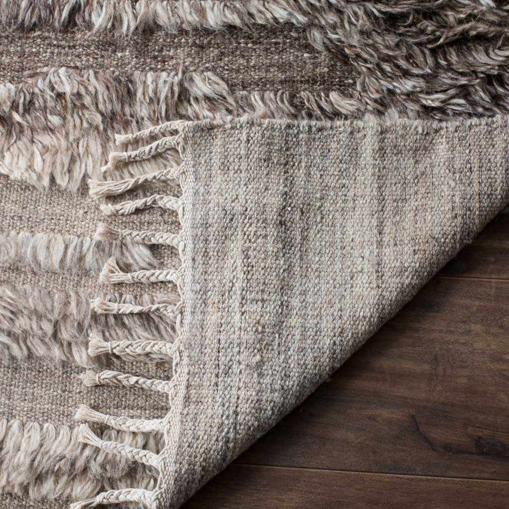 A folded rug edge reveals tightly woven backing beneath the thick gray and ivory pile