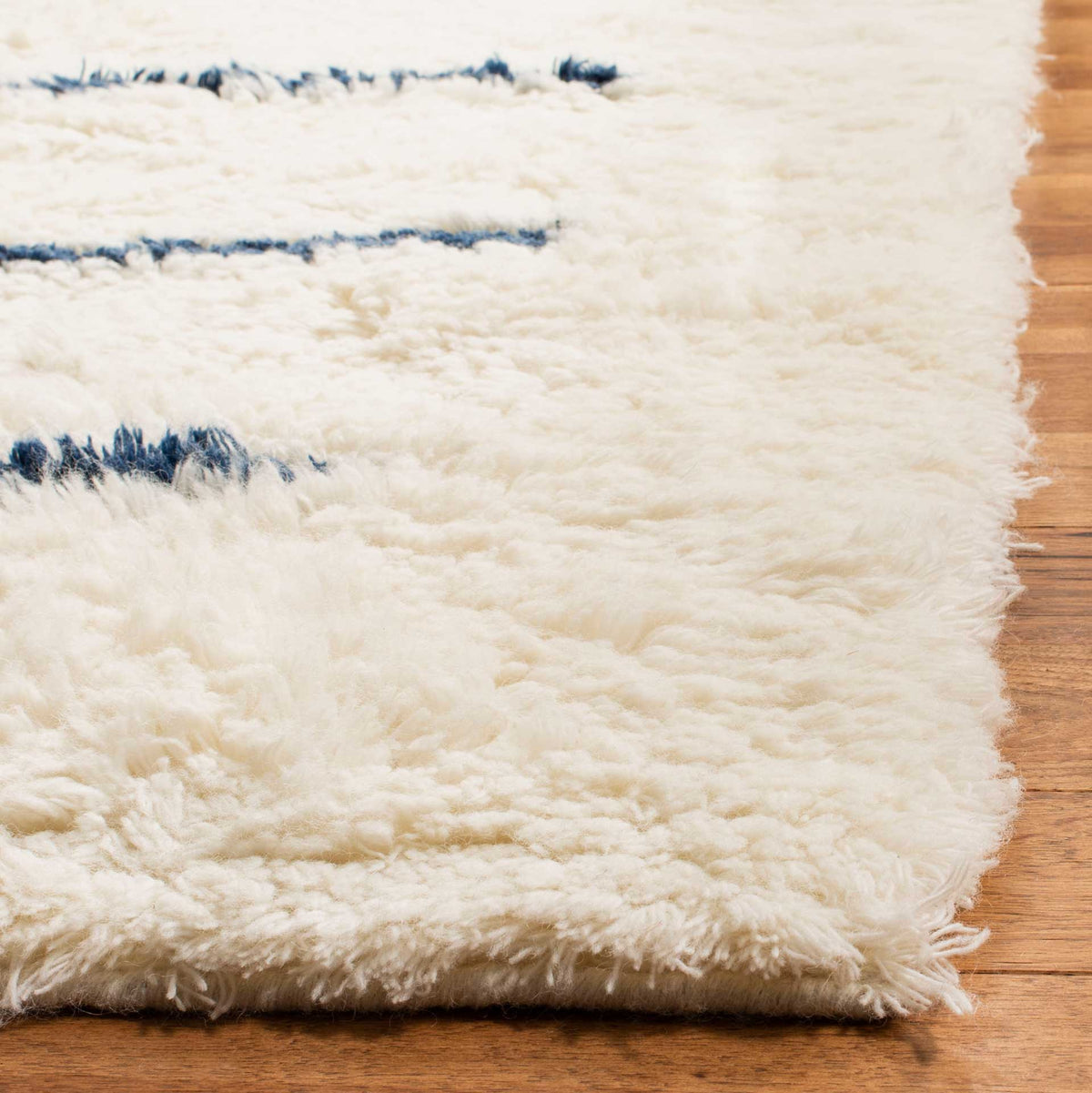 Thick ivory wool fibers soften the rug's edge beside deep navy stripe accents.