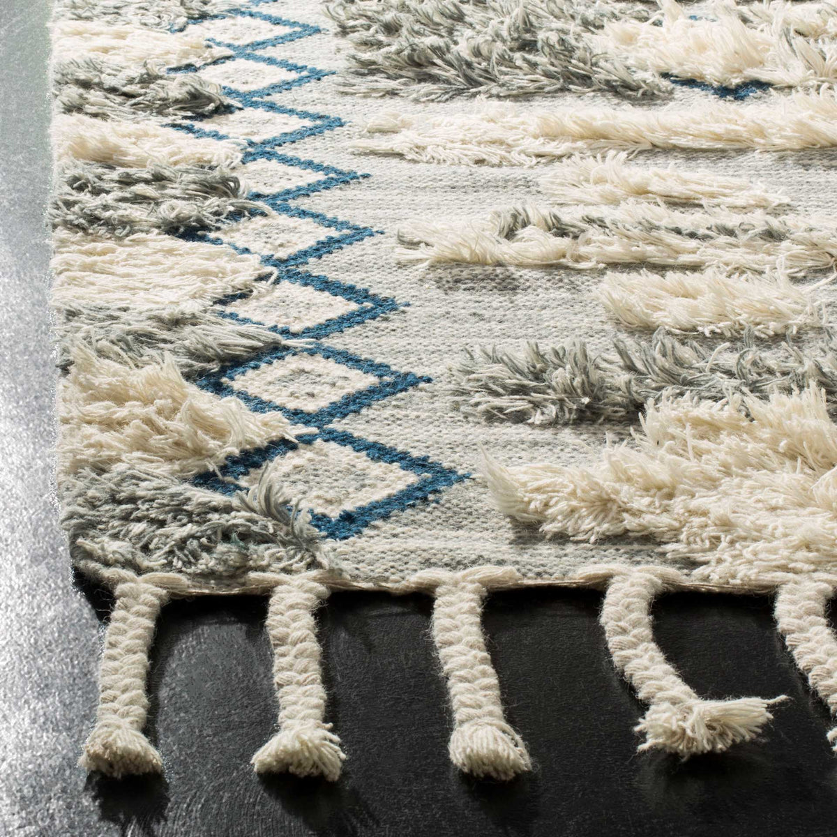 Raised gray and ivory tufts, blue diamond trim, and knotted fringe add a tactile finish