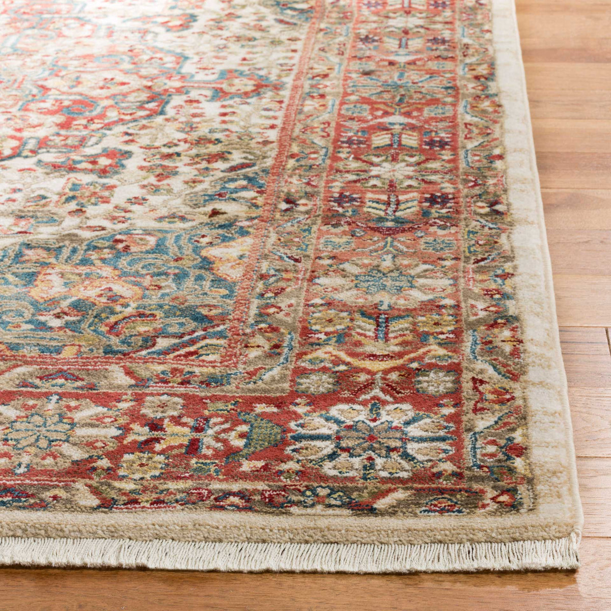 Soft ivory fringe and a densely patterned floral border add texture to the red and blue rug