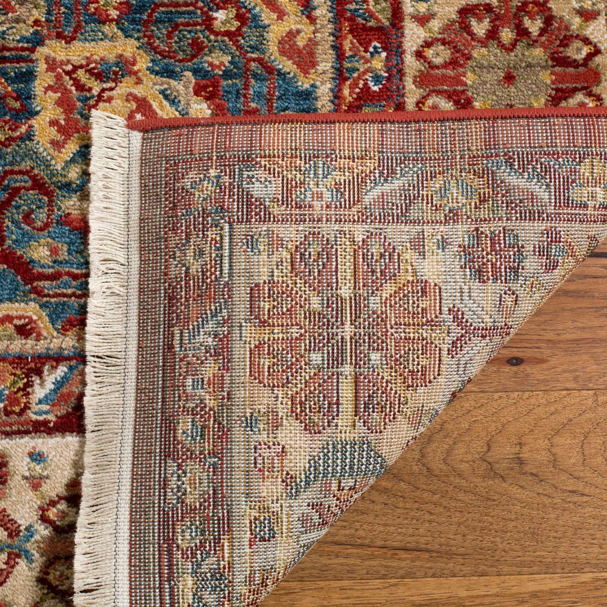 Woven backing reveals the ornate pattern beneath the red rug, finished with a pale fringe